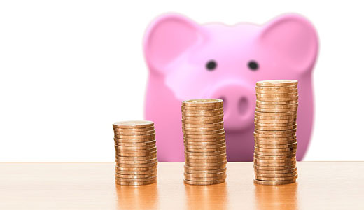 Coins stacked on a table with a pig money bank in the background