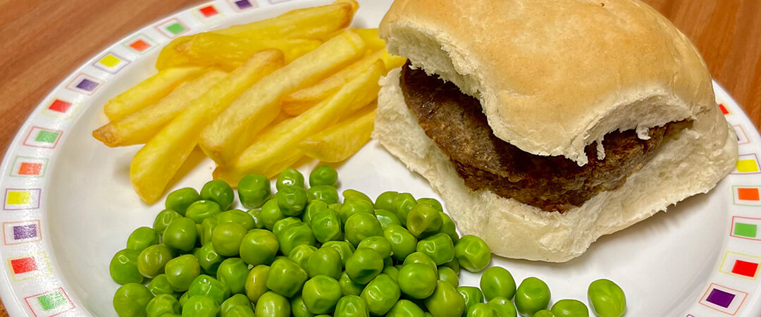 Beefburger in a bun served with chips and peas