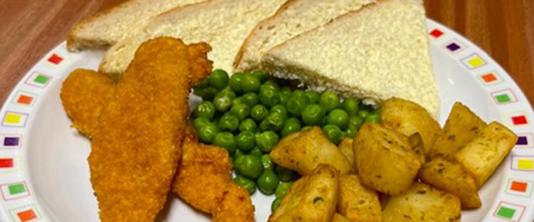 Chicken goujons served with herby diced potatoes, peas, bread and spread