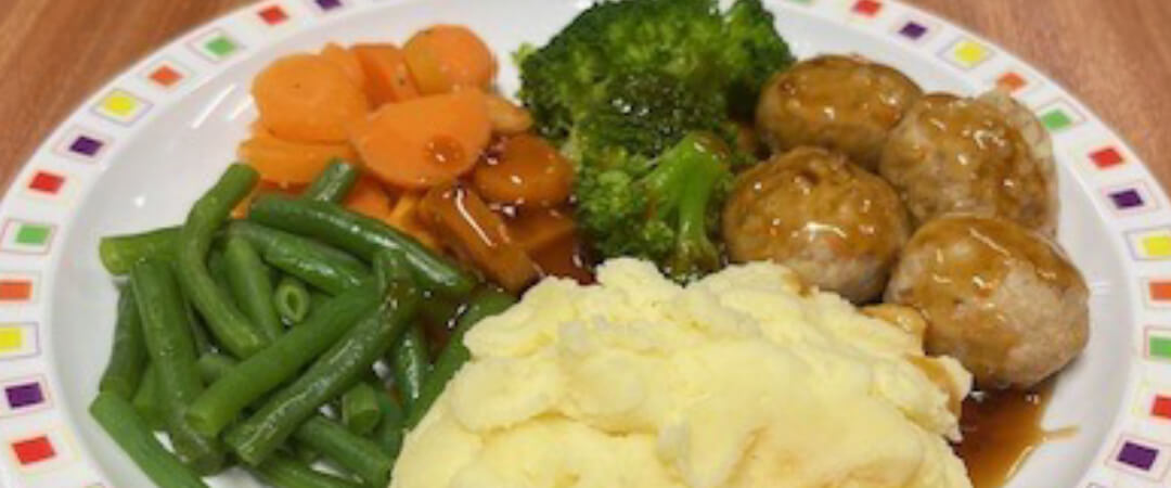 Pork and carrot meatballs in gravy served with mashed potato, broccoli, carrots, green beans and gravy