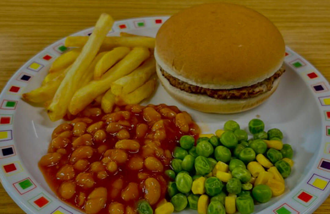 Beefburger in a bun served with chips and peas