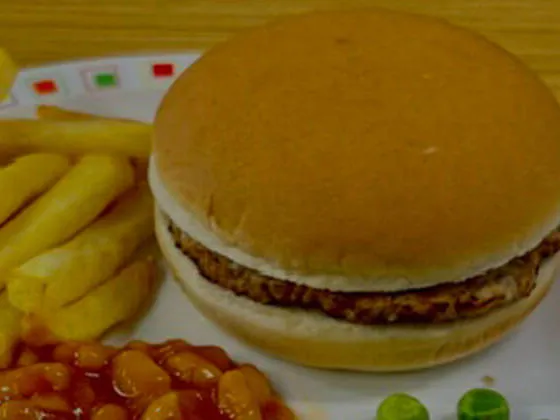 Beefburger in a bun served with chips and peas