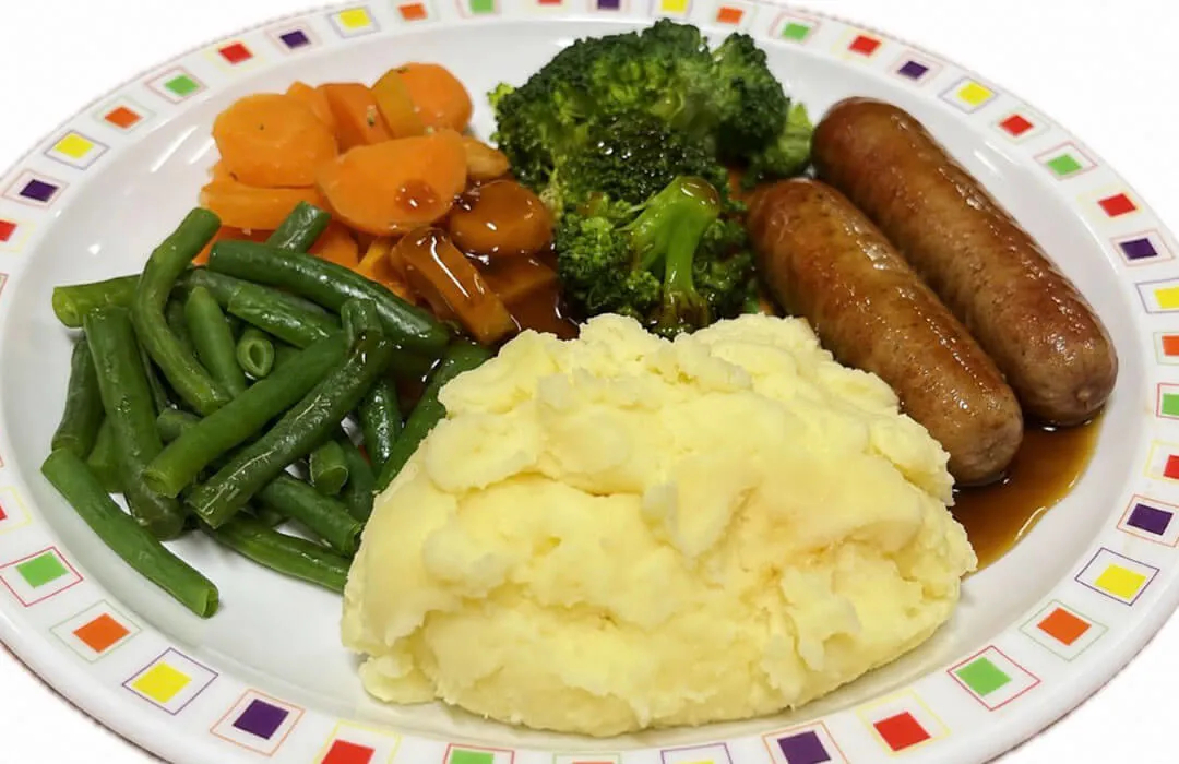 Pork sausage served with mashed potato, carrots, broccoli and gravy