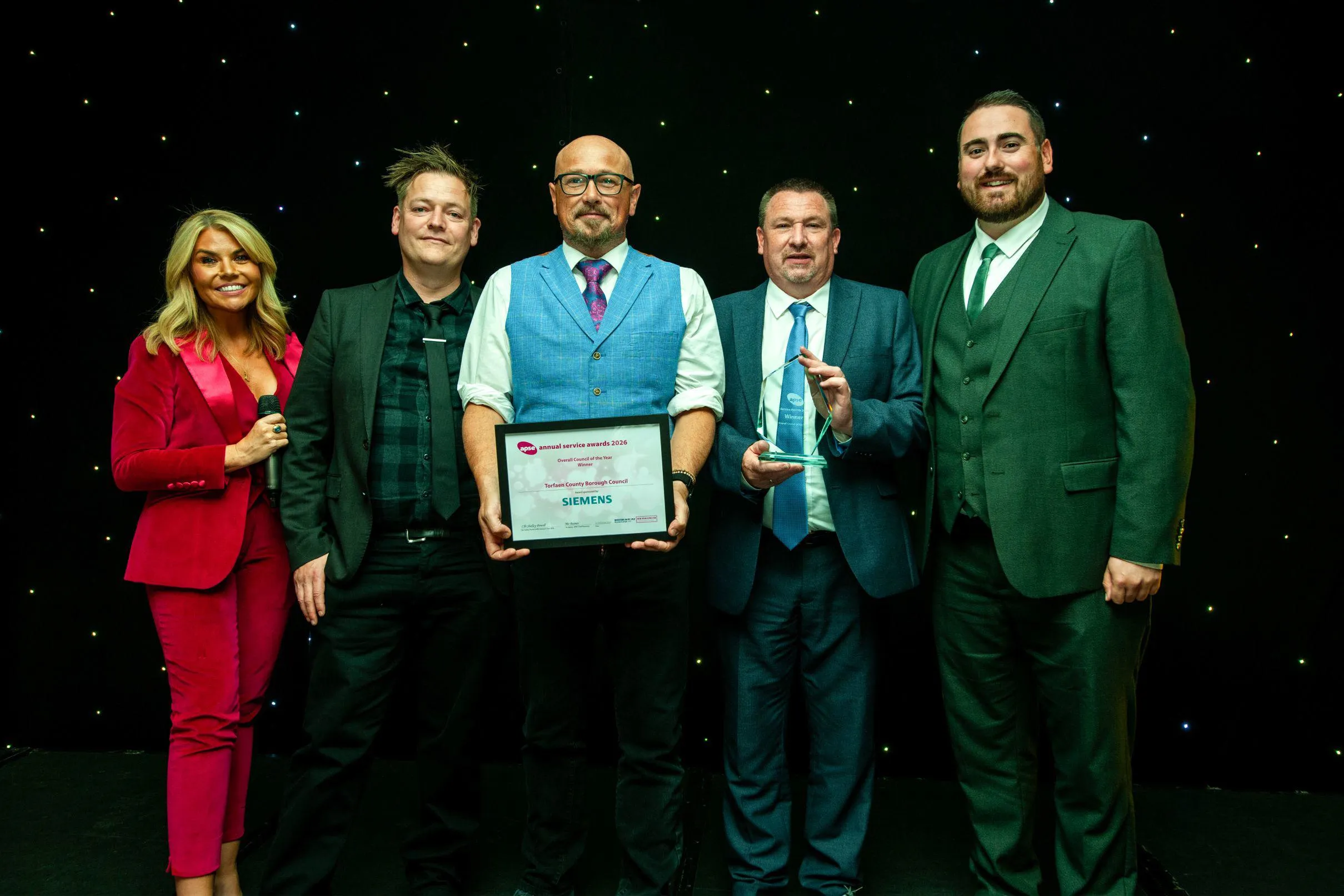 Three members of the council stood on a stage holding an award next to another man and female host