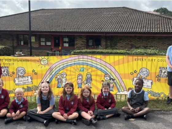 A group of school children in uniform stand and sit in front of a colorful banner outside Henllys Church in Wales school