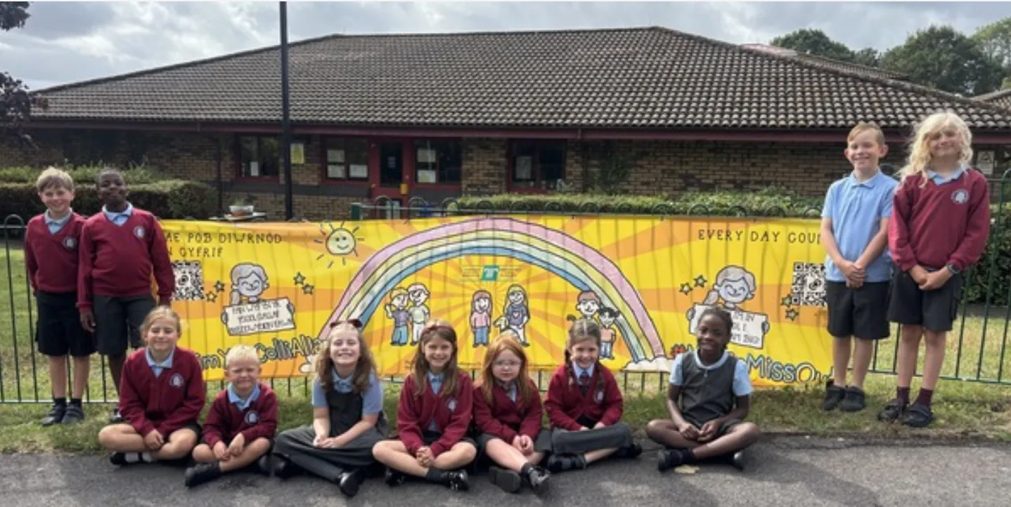 A group of school children in uniform stand and sit in front of a colorful banner outside Henllys Church in Wales school
