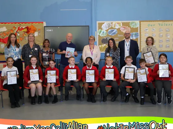 A group of New Inn Primary School pupils holding up copies of the books front cover artwork, alongside staff.