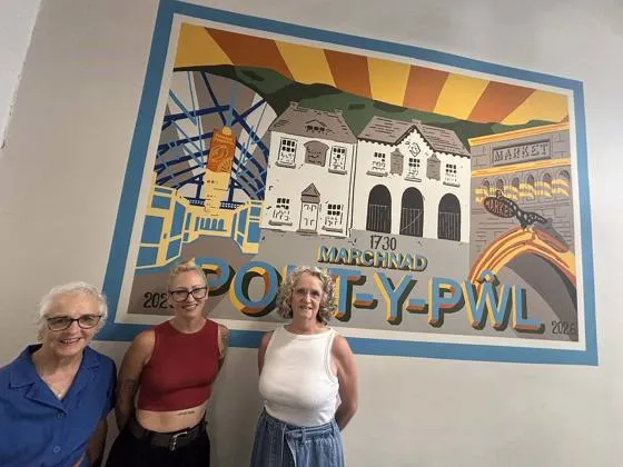Three people standing in front of a mural featuring local landmarks