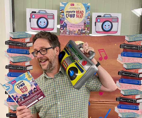 Man holding an inflatable music player, surrounded by colourful books