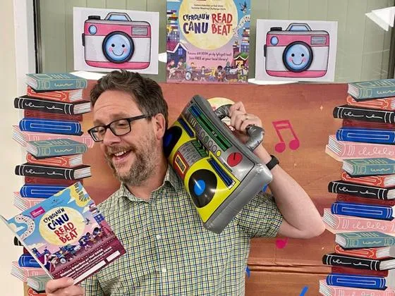Man holding an inflatable music player, surrounded by colourful books