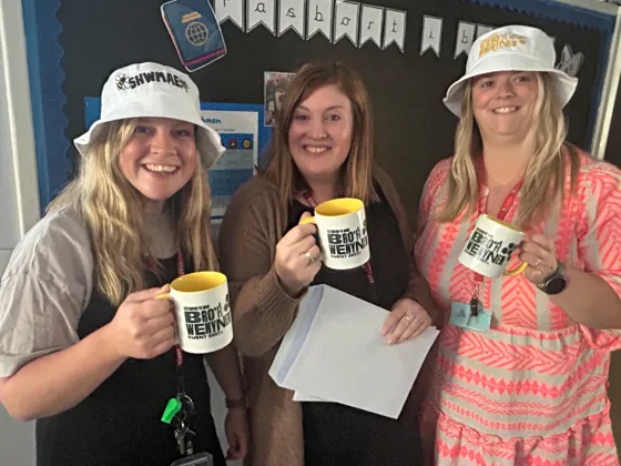 Three woman smiling holding mugs and wearing hats promoting the Urdd Eisteddfod Bro'r Wenynen Gwent